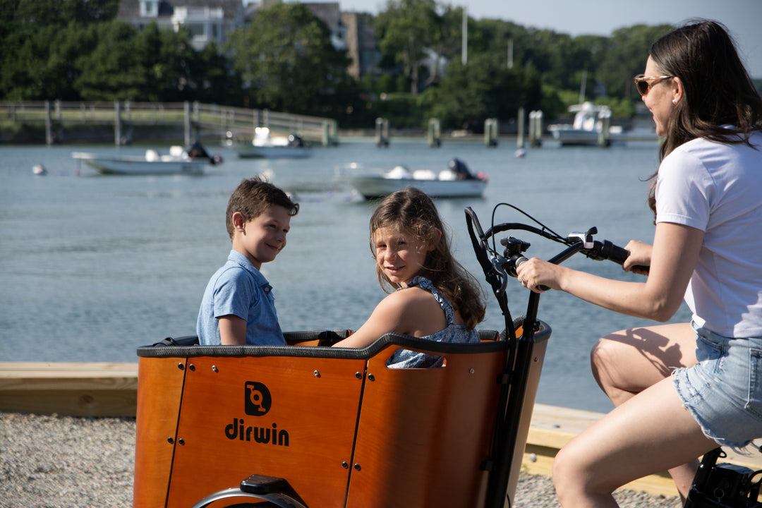Woman riding a cargo bike with two children in a waterfront setting
