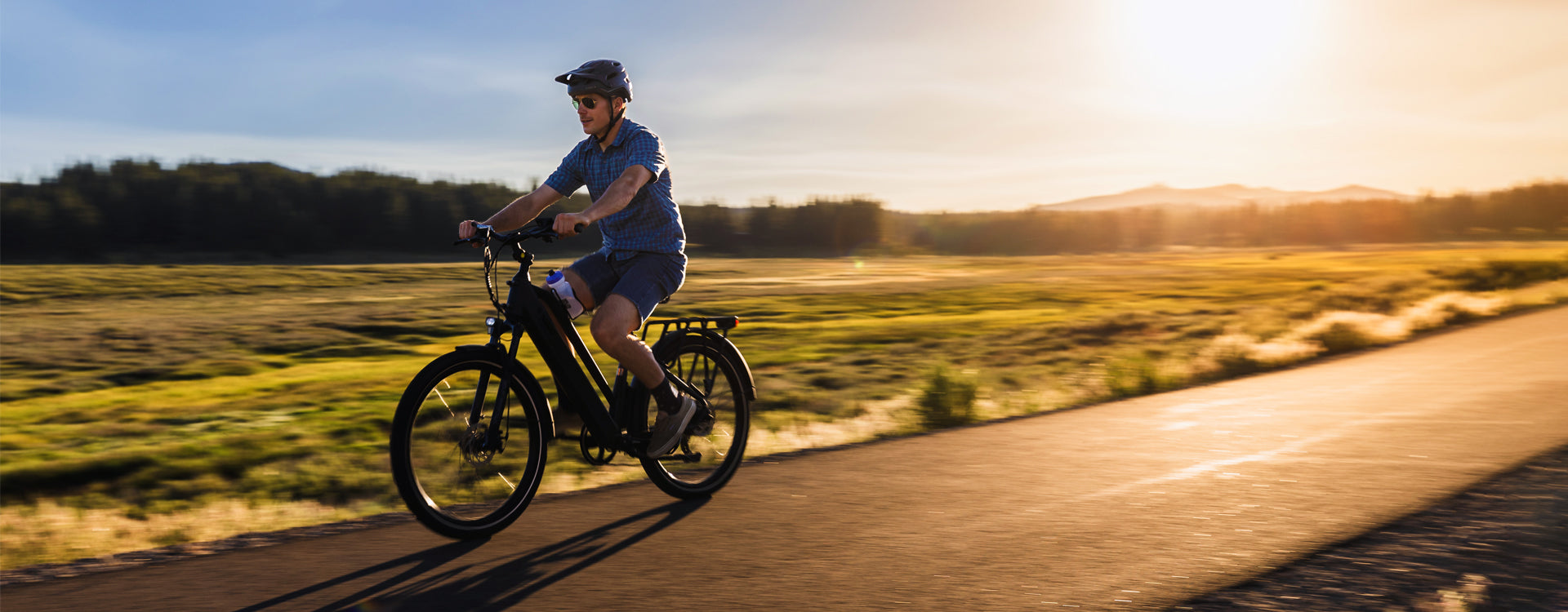 Person riding an electric bike on a scenic country road at sunset with mountains in the background.