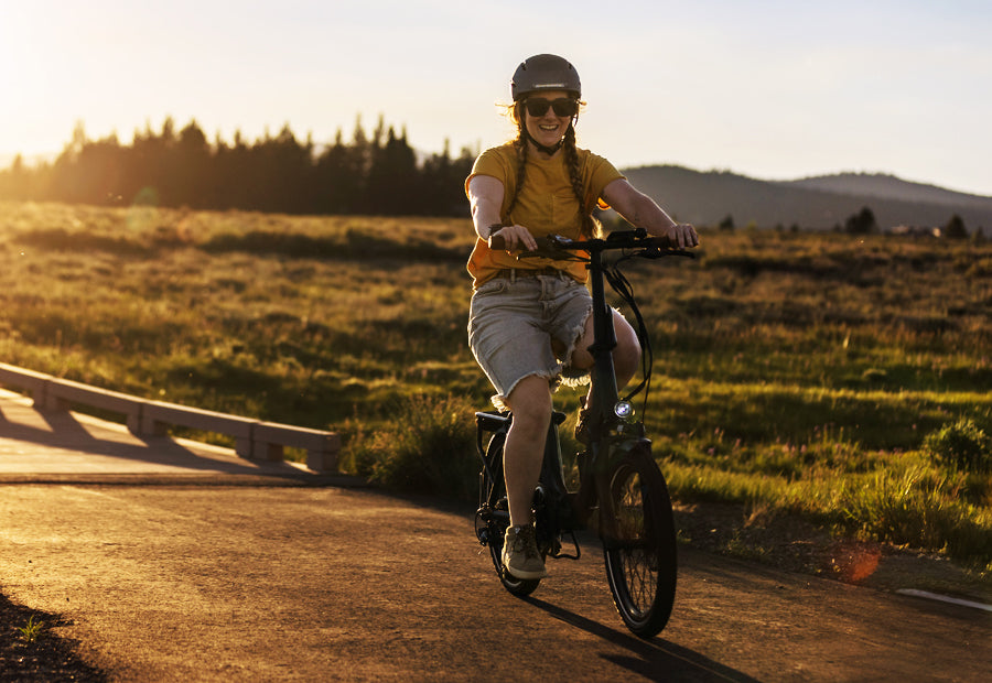 Person riding a bicycle on a rural path at sunset wearing a helmet and sunglasses.