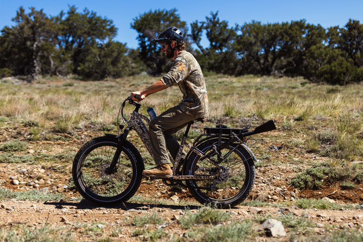 Riding the Dirwin Pioneer Plus Fat Tire Electric Bike offroad desert camouflage with a outdoor landscape background