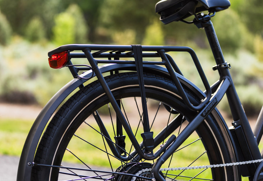 Rear view of an electric bicycle with a sturdy cargo rack and red reflector, parked outdoors on a sunny day.