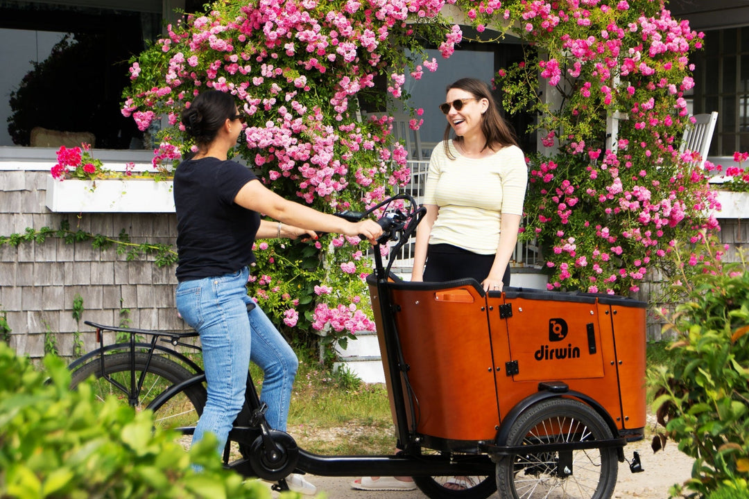 Two people with a cargo bike in front of a house with pink flowers.